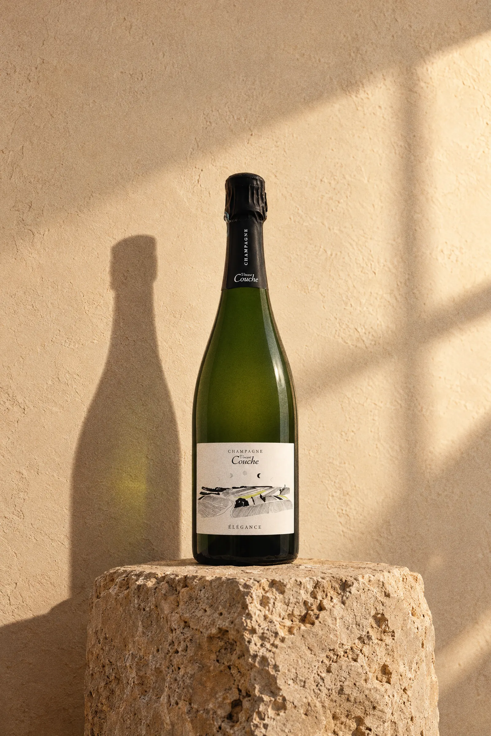 Champagne Vincent Couche Elegance Brut Nature bottle standing on a stone plinth in warm light